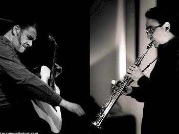 Schwarz-Weiß-Bild: 1 Mann spielt Gitarre, 1 Saxophon