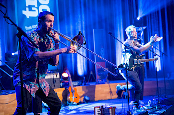 Zwei Musiker mit Trompete und E-Gitarre auf einer blau beleuchteten Bühne