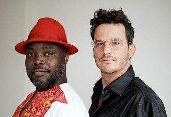 1 afrikanischem Mann mit rotem Hut und 1 europäischer Mann mit schwarzem TShirt