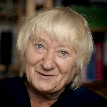 Eine ältere Frau mit kurzen hellblonden Haaren schmunzelt in die Kamera