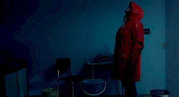 1 Frau steht in der Dunkelheit. Sie trägt einen roten Regenjacke