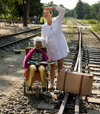 An der Gleisbahn wartet eine Frau mit einer Puppe