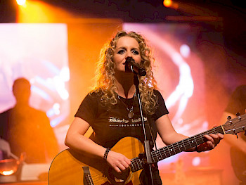 Eine blonde Sängerin singt auf der Bühne mit der Gitarre