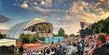 Open-Air-Bühne mit weißem Kuppeldach und Publikum im Sommer