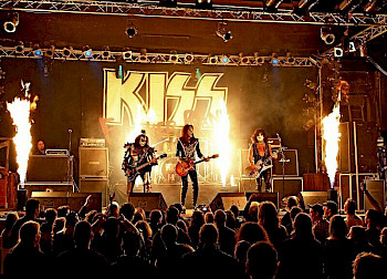 Rocker machen Musik auf der Bühne, hinter ihnen steht Schrift KISS