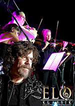 Hinter Phil Bates spielen die Musiker Geige in lilaer Licht