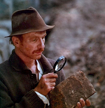 ein Mann schaut einen Stein mit der Lupe