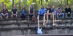 Schüler mit E-Gitarren und Blechblasinstrumenten sitzen auf einer Treppe open air