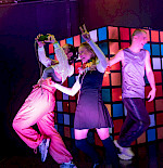 3 Jugendlichen spielen vor einem großen Rubik