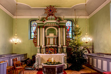 Blick auf einen Altar, hellgrüne Wände drumherum, Weihnachtsbaum neben dem Altar
