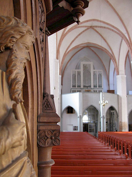Blick auf einen weißen Altar in der Kirche, links Steinfigur, rote Sitze
