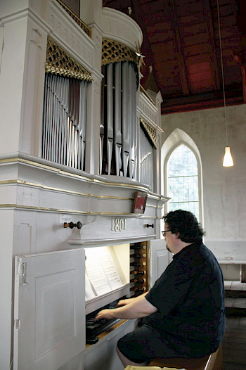 schwarz gekleidertert Organist sitzt an weißer Orgel
