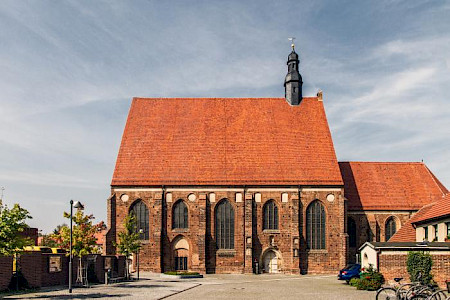 Backstein-Kirche von der Seite, mit großen dunklen Fenster vor einem blauen Himmel