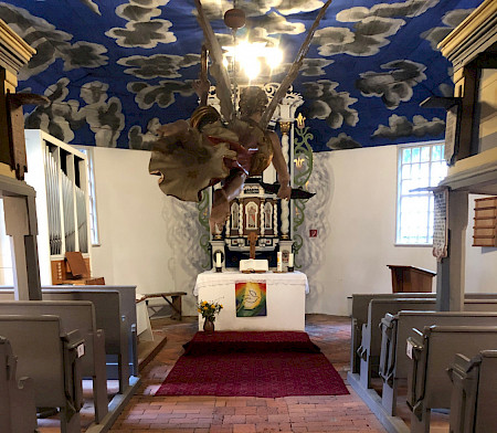 Kircheninnenraum mit Wolkenbemalung und aufgehängtem Taufengel an der Decke